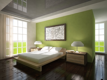 room with a hardwood floor, bright
               windows on two sides, and a two-person bed with a bedside table and lamp on each side